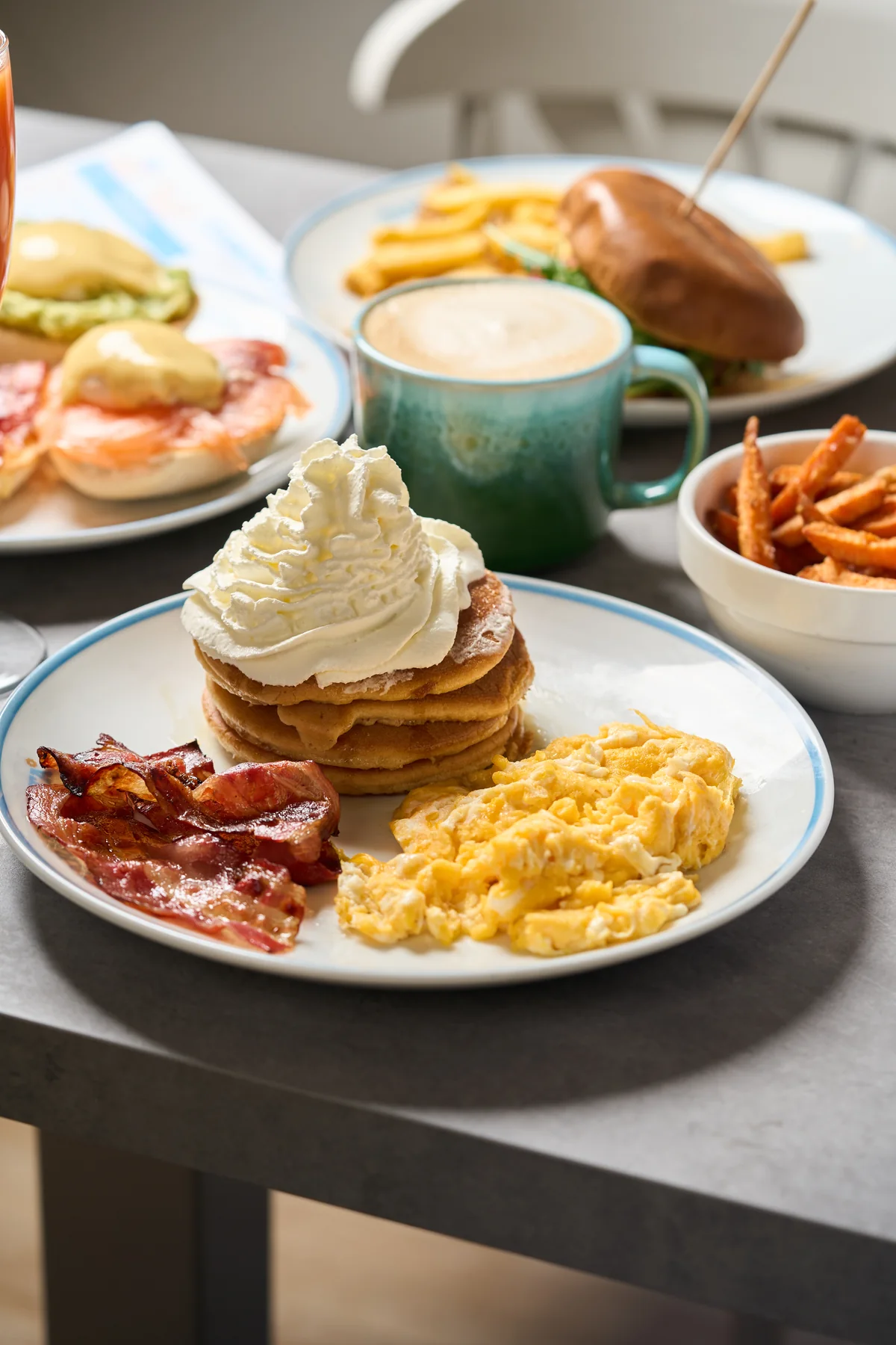 Pancakes con nata, huevos revueltos, bacon y café en una mesa de Carmencita Brunch